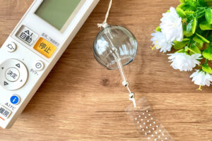 木製テーブルの上にあるエアコンのリモコン、風鈴、白い造花